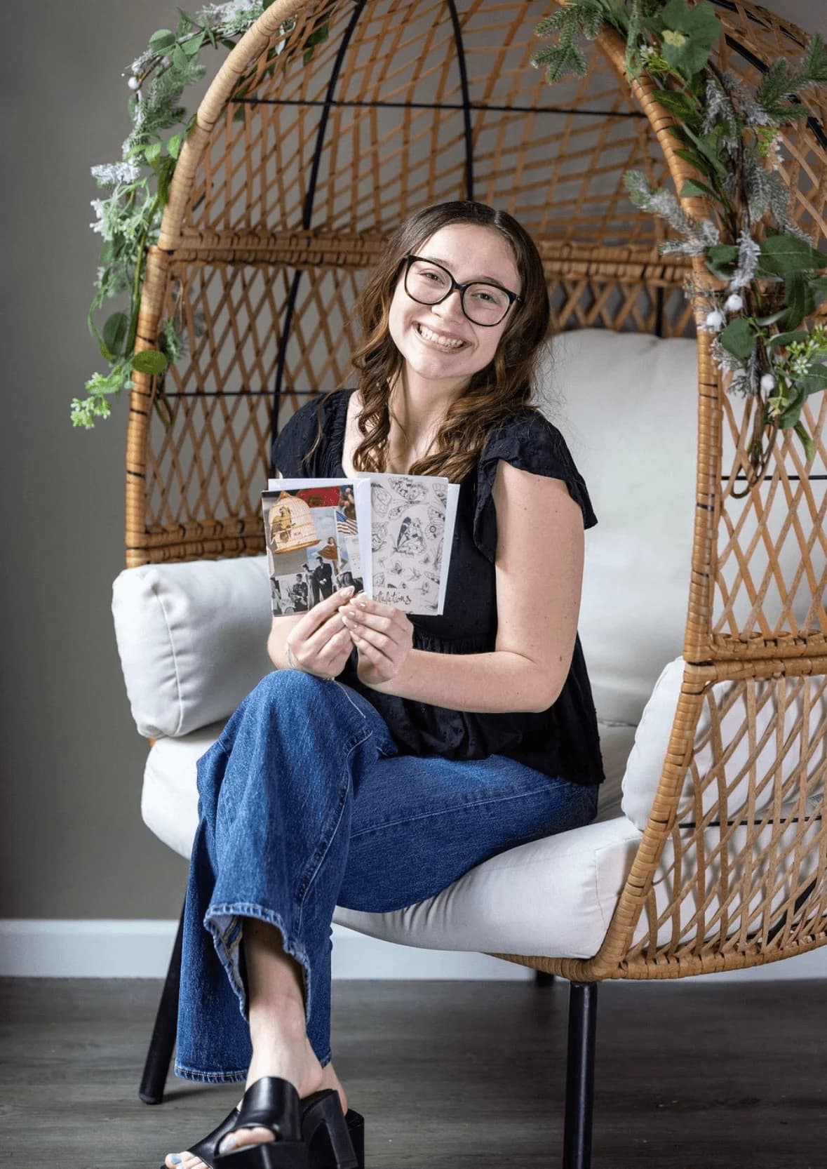 Claire smiling in a wicker chair while holding her handmade cards